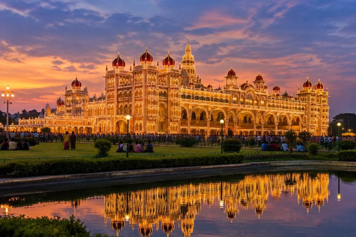 Mysore Palace lit up with thousands of bulbs at dusk, reflected in a pool
